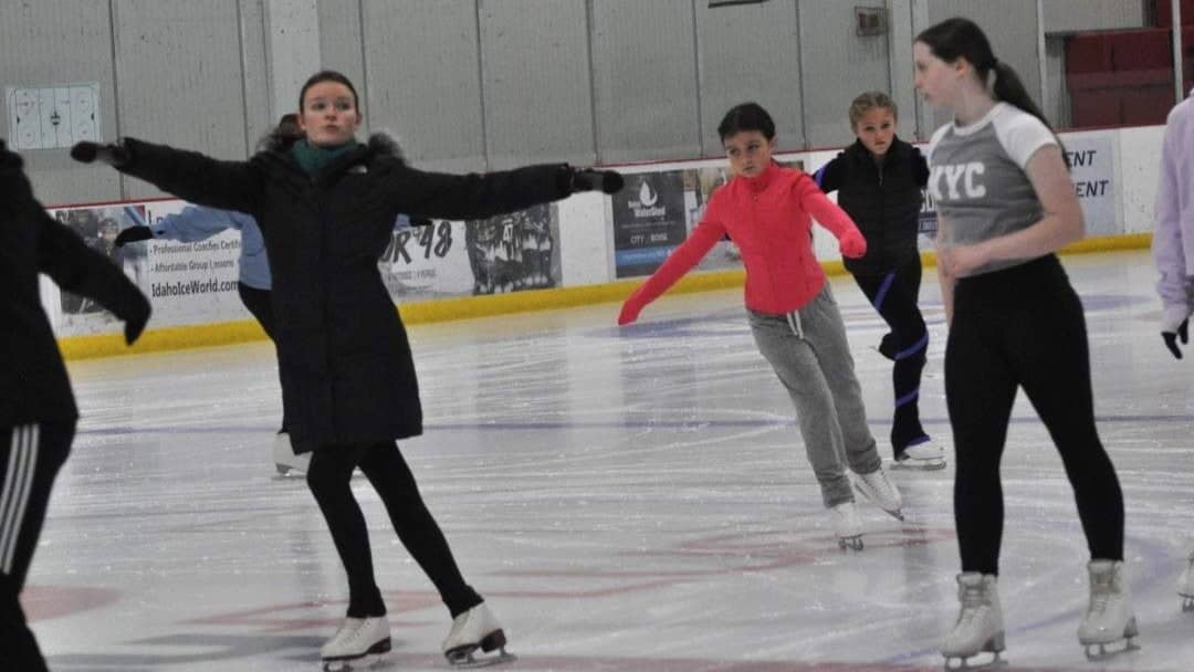 Coach Cadence Brunzlick, dressed in all black, with arms extended, teaches dance moves to students. 